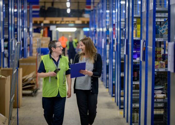 Two staff members in a warehouse discussing job uncertainty for warehouse staff